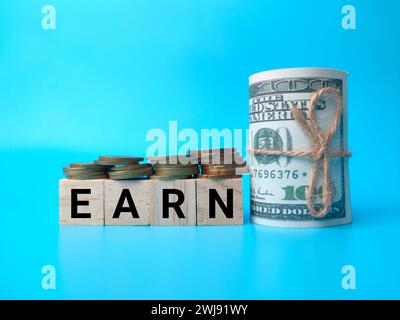 Holzblock, Münzen und Banknoten mit Text VERDIENEN auf blauem Hintergrund. Stockfoto