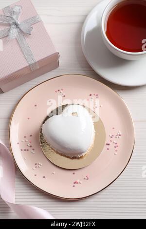 St. Valentinstag. Köstlicher herzförmiger Kuchen, Tee und Geschenk auf weißem Holztisch, flach gelegen Stockfoto
