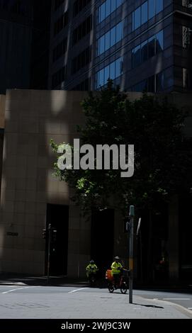 Zwei Fahrer überqueren die Bent St am Farrer Place, in einem Sonnenlicht zwischen tiefen Schatten im CBD von Sydney Stockfoto