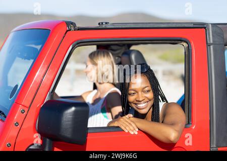 Zwei Frauen teilen Freude auf einem sonnigen Roadtrip in einem roten Jeep. Stockfoto