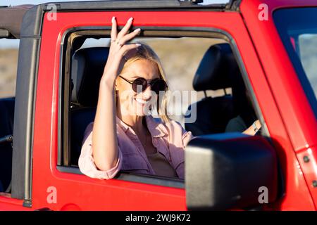 Junge kaukasische Frau genießt eine sonnige Fahrt in einem roten Fahrzeug auf einer Autofahrt Stockfoto