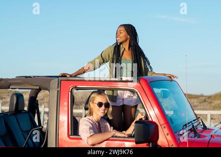 Zwei Frauen teilen Freude auf einem sonnigen Roadtrip in einem roten Jeep. Stockfoto