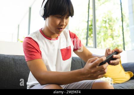 Teenager Asian Boy spielt zu Hause gern, konzentriert und trägt Kopfhörer Stockfoto