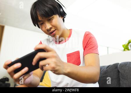 Teenager Asiatische Junge spielt zu Hause ein mobiles Spiel, voll engagiert Stockfoto