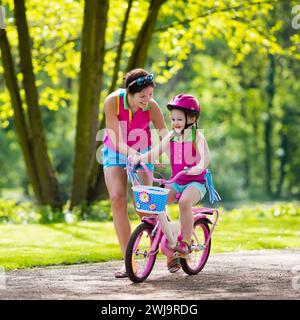 Kinderfahrrad. Kind auf Fahrrad im sonnigen Park. Mutter bringt dem kleinen Mädchen das Radfahren bei. Vorschulkinder lernen, mit einem sicheren Helm ins Gleichgewicht zu kommen. Stockfoto