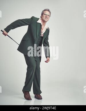 Reife, Mann und Mode mit Peitsche im Studio mit Anzug auf grauem Hintergrund und Vintage-Look. Tuxedo, Eleganz und Retro mit Reiterbesatz und formellem Design Stockfoto
