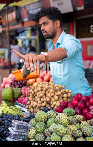 Ein junger Indianer verkauft Obst in seinem Laden auf einem lokalen Markt Goa India. Mann, der Gemüse und Obst an Kunden auf einem Markt auf dem Goa Bazar verkauft. Stre Stockfoto