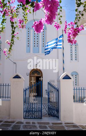 Blick auf die griechische Flagge, die in der Luft winkt, neben einer Bougainvillea und einer weiß getünchten Kirche im Hintergrund in iOS Griechenland Stockfoto