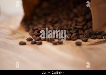 Tisch, Nahaufnahme und frisch geröstete Kaffeebohnen, die aus einer Papiertüte auf eine alte Holztheke mit Kopierraum verschüttet werden. Studio, aromatisches Bitterkoffein Stockfoto