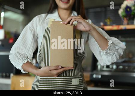 Lächelnde Kaffeehausbesitzerin mit brauner ökologischer Verpackung. Umweltfreundliche Produkte und Zero Waste-Konzept Stockfoto