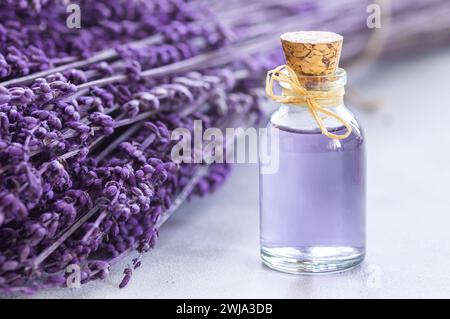 Glasflasche ätherisches Lavendelöl mit getrockneten Lavendelblüten und Samen auf weißem Tisch, Aromatherapie-Spa-Massagekonzept. Lavendula oleum Stockfoto