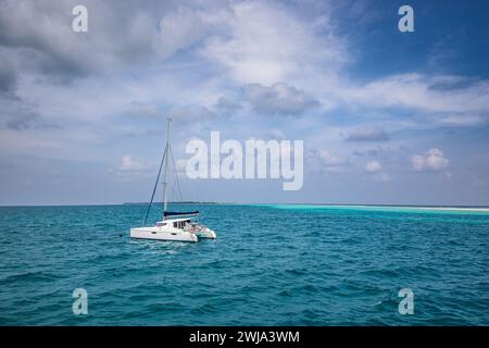 Wunderschönes türkisfarbenes Wasser rund um das weiße Luxussegelboot, das mitten im Ozean ankert. Bewölkter Himmel, Lagune des Ozeans. Abenteuerreisen, entspannende Meereslandschaft Stockfoto