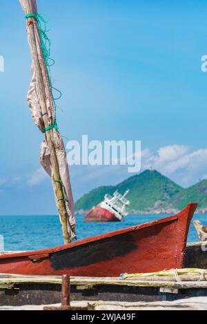 Ein traditionelles rotes Fischerboot steht vor einem geerdeten Schiff vor der Küste von Bahia Santana und zeigt den Kontrast zwischen Kleinfischerei und mar Stockfoto
