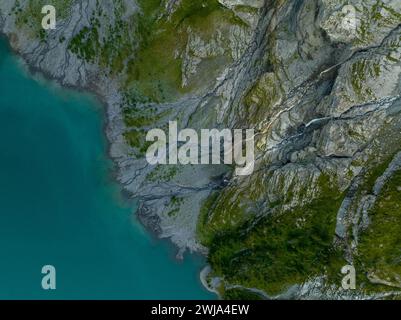 Aus der Vogelperspektive auf einen abgeschiedenen Bergsee mit kristallklarem türkisfarbenem Wasser, eingebettet zwischen zerklüfteten Klippen und Grün. Stockfoto