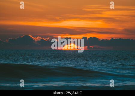 Malerischer Blick auf den farbenfrohen Sonnenuntergang mit bewölktem orangefarbenen Himmel über dem plätschernden Meer am Abend in der Natur auf dem Land Stockfoto