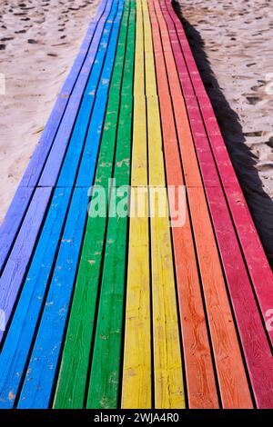 Holzweg zum Strand mit blauen grünen gelben orange und roten Farben an der Sandküste am sonnigen Tag in Penon de Ifach in Calpe, Alicante, Spanien Stockfoto