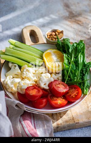 Eine gesunde Schüssel mit frischem Gemüse mit Gurkenscheiben, Kirschtomaten, Blumenkohlröschen, einem Zitronenkeil und Rucolablättern auf einem Holzschwein Stockfoto