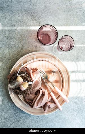 Von oben geschmackvolle Osterkarte mit pastellfarbenem Geschirr und dekorativen Eiern in einem kleinen Nest, begleitet von elegantem Besteck. Stockfoto