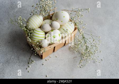 Eine bezaubernde Sammlung bemalter Ostereier mit Streifen und Punkten, eingebettet in einen Korb mit zarten Frühlingsblumen Stockfoto