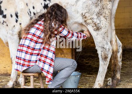 Junge Bäuerin melkt eine Milchkuh manuell. Tierschutz und Pflege auf einem Bio-Bauernhof. Stockfoto