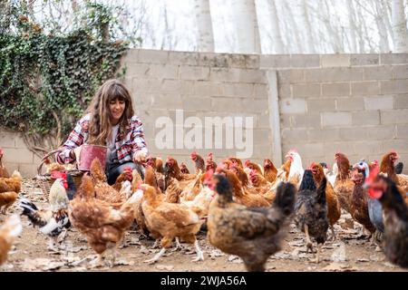 Glückliche junge Bäuerin, die Hühnern mit der Hand Mais zufüttert. Tierschutz und Pflege auf einem Bio-Bauernhof. Stockfoto