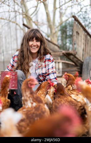 Glückliche junge Bäuerin, die Hühnern mit der Hand Mais zufüttert. Tierschutz und Pflege auf einem Bio-Bauernhof. Stockfoto