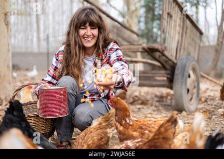 Glückliche junge Bäuerin, die Hühnern mit der Hand Mais zufüttert. Tierschutz und Pflege auf einem Bio-Bauernhof. Stockfoto