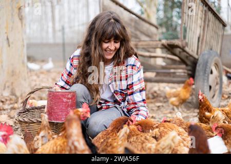 Glückliche junge Bäuerin, die Hühnern mit der Hand Mais zufüttert. Tierschutz und Pflege auf einem Bio-Bauernhof. Stockfoto