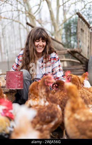 Glückliche junge Bäuerin, die Hühnern mit der Hand Mais zufüttert. Tierschutz und Pflege auf einem Bio-Bauernhof. Stockfoto