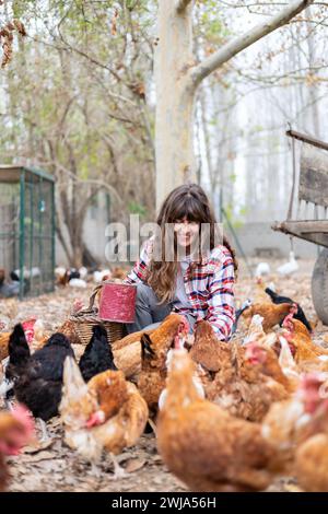 Glückliche junge Bäuerin, die Hühnern mit der Hand Mais zufüttert. Tierschutz und Pflege auf einem Bio-Bauernhof. Stockfoto