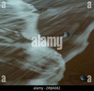 Ruhige Strandszene mit sanften Wellen über Sandstrand und Felsen Stockfoto