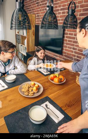 Ein Elternteil serviert lächelnde Kinder an einem Familienfrühstück mit gesunden Speisen in Scheiben geschnittenes Obst Stockfoto