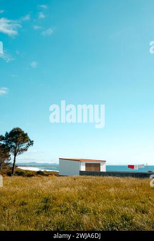 Eine ruhige Szene in Larino, Galicien, Spanien, mit einem einstöckigen weißen Gebäude vor einem leuchtend blauen Himmel, mit Wäschetrocknung und üppigem Grasnebel Stockfoto