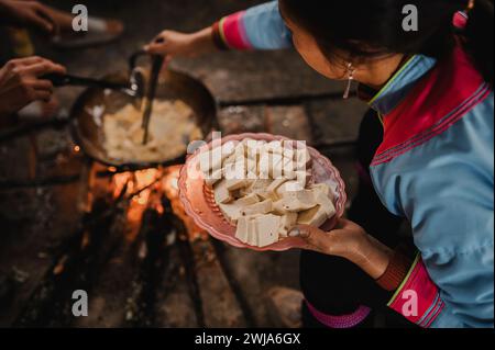 Von oben anonym von Menschen in traditioneller Kleidung, die auf Holzbank sitzen, während sie in der alten Küche Vietnams Essen kochen Stockfoto