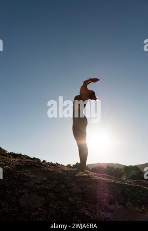 Seitenansicht einer schlanken Frau in Sportbekleidung, die mit aufsteigender Salute-Yoga-Pose steht und während des Sonnenaufgangs Hastasana auf dem Hügel vor grauem Himmel ausführt Stockfoto