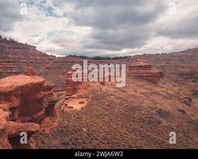 Blick von oben auf nicht erkennbare Reisende, die auf einem schmalen Pfad auf dem Hügel des Berges vor bewölktem Himmel im spanischen Badlands-Tal spazieren Stockfoto