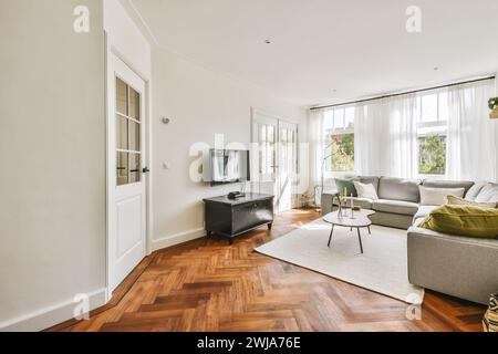 Ein helles, luftiges Wohnzimmer mit großen Fenstern, Hartholzböden und komfortablen modernen Möbeln bei warmem Tageslicht. Stockfoto