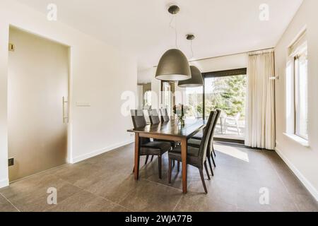 Moderner Speisesaal mit elegantem Tisch, großen Fenstern und stilvollen Pendelleuchten. Stockfoto