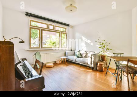 Ein gut beleuchtetes Wohnzimmer mit gemütlichem Sofa, Esstisch aus Holz und aufrechtem Klavier am Fenster, das Wärme und Komfort ausstrahlt Stockfoto