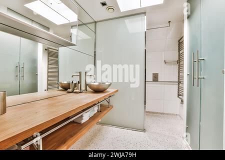 Ein elegantes, modernes Badezimmer mit Holzwaschtisch, Duschtüren aus Glas und mit Tageslicht beleuchteten Metallarmaturen. Stockfoto