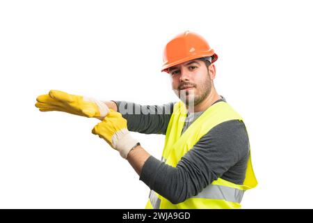 Männlicher Baumeister Erwachsener lächelnd trägt orangefarbenen Helm und fluoreszierende Weste, die auf gelben Sicherheitshandschuh aufsetzt und sich für die Arbeit vorbereitet, isoliert auf weiß Stockfoto