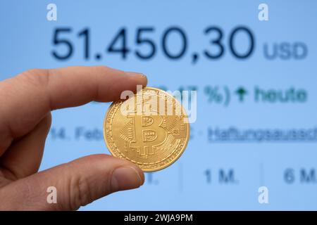 Bitcoin-Münze zwischen den Fingern vor einem Marktpreis von über 50.000 USD Stockfoto