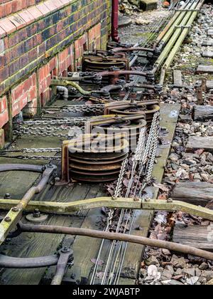 Riemenscheiben und Ketten von einem Eisenbahnstellwerk an der Seite der Eisenbahnstrecken in Großbritannien Stockfoto