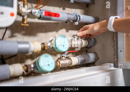 Die Hand einer Frau schließt eine Warmwasserleitung, um Geld zu sparen, Wasserzähler kaltes und heißes Wasser, Wasserverbrauch in echten Wohnungen in Europa Stockfoto