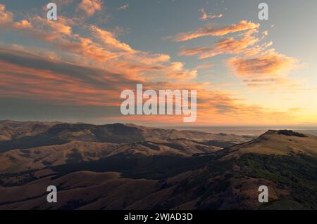 Der Himmel ist mit einem bunten Nachglühen erfüllt, während die Sonne über einer atemberaubenden Landschaft aus sanften Hügeln und Wolken untergeht Stockfoto