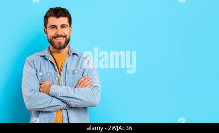 Glücklicher Millennials steht selbstbewusst mit gekreuzten Armen im Studio Stockfoto