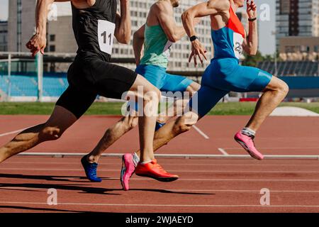 Drei männliche Athleten sprinten auf der roten Bahn, Muskeln gespannt, hart im Wettkampf Stockfoto