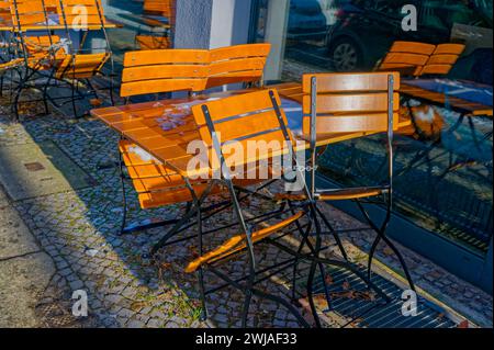 Winterszene mit Holzmöbeln auf dem Bürgersteig vor einem Restaurant mit Schnee auf dem Tisch und angeketteten Stühlen. Stockfoto