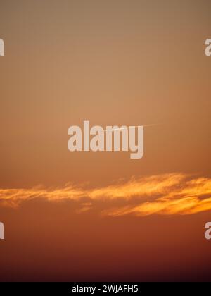 Ein Flugzeug, das durch einen atemberaubenden orangefarbenen Sonnenuntergangshimmel fliegt. Stockfoto