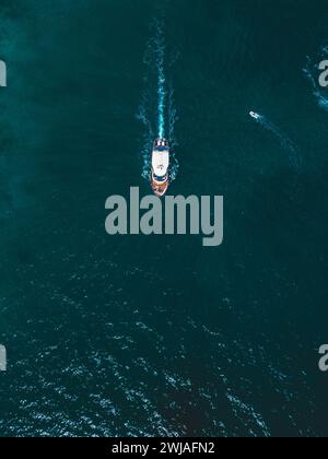 Ein Blick aus der Vogelperspektive auf ein weißes und braunes Boot, das mit anderen kleinen Booten auf dem Wasser segelt. Stockfoto